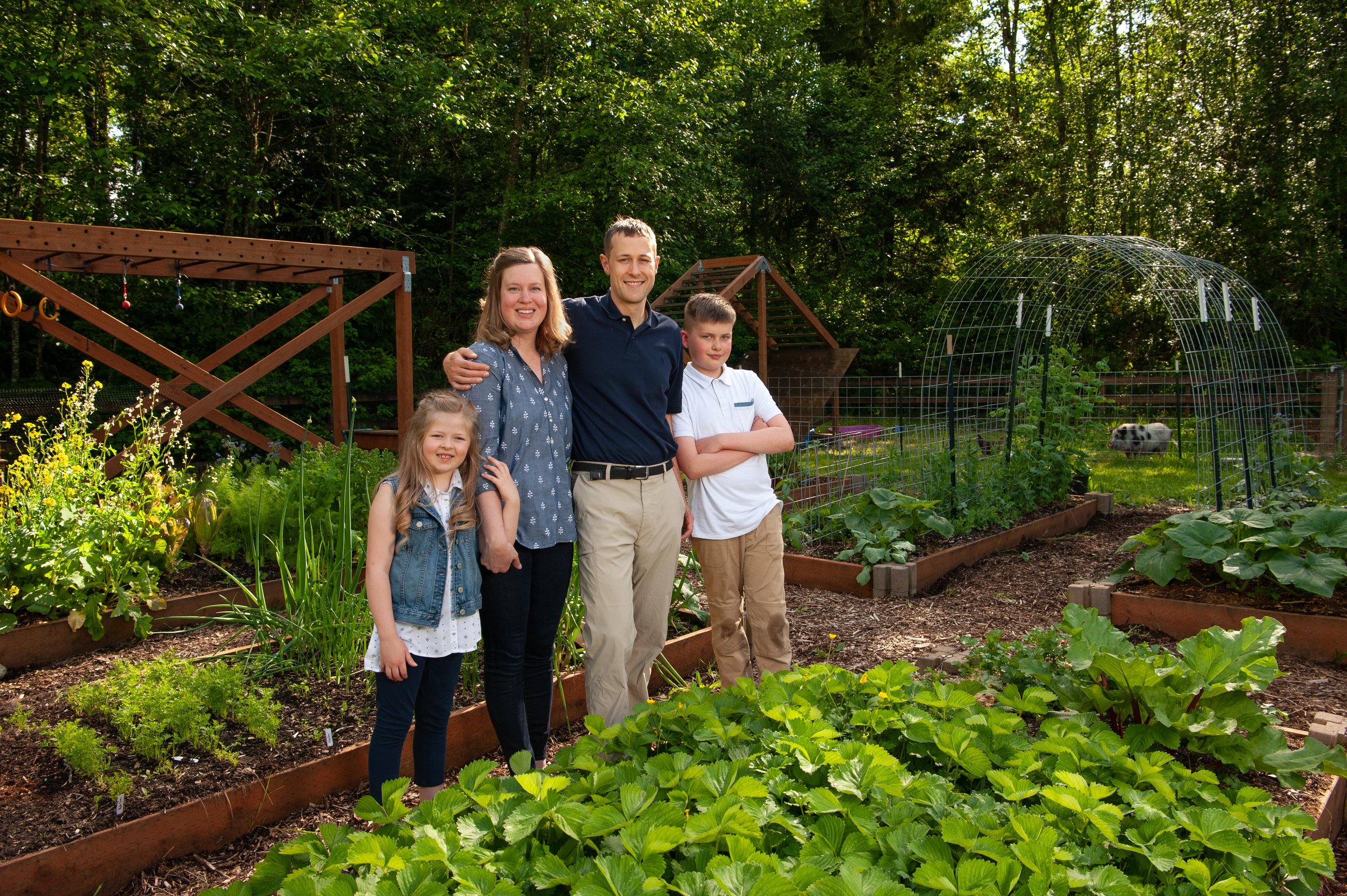 Family standing together in a lush home garden, surrounded by vibrant vegetable beds and greenery, showcasing a healthy lifestyle and gardening activities.
